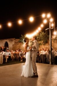 Bride and groom sharing their first dance beneath romantic festoon lights during an outdoor wedding reception at Metohi Istoria, a historic Venetian estate in Chania, Crete.