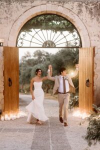 Bride and groom making their grand entrance through the historic Venetian gate at Metohi Istoria during a destination wedding in Chania, Crete.